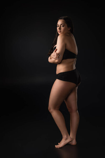 Full length view of plus size girl hidding body with shame on black background