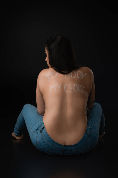 Back view of plus size model with lettering My Body My Choice on naked back sitting on black background