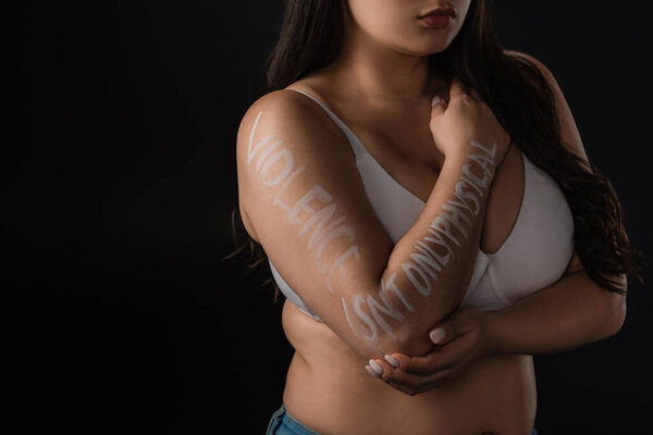 Cropped view of plus size model covering bust with hand with lettering Violence is not Only Physical isolated on black