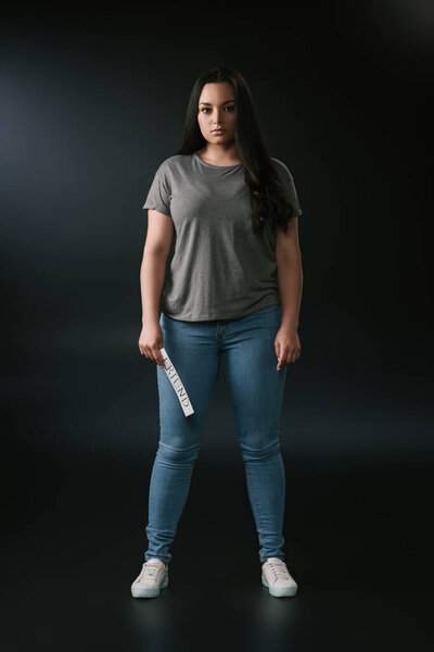 Вид спереди красивой девушки plus size, держащей открытку с буквами на чёрном фоне

