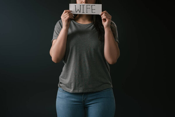 Cropped view of plus size girl holding card with word wife on black background