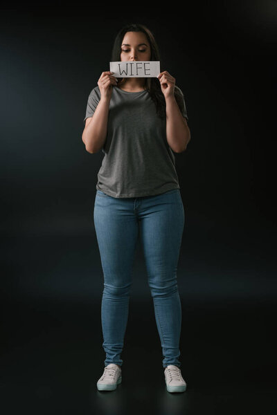 Полный вид девушки plus size, держащей открытку со словом "жена" на черном фоне
