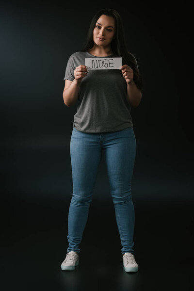 Вид улыбающейся девушки в полный рост с карточкой судьи на чёрном фоне
