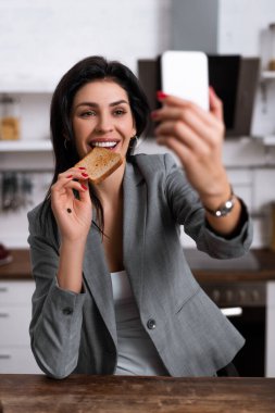Avuç içlerine siyah noktalı gülümseyen bir kadının lezzetli tost ekmeği yemesi ve selfie çekmesi, aile içi şiddet kavramı. 
