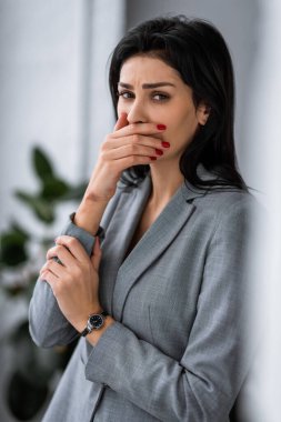 upset businesswoman with bruise on hand covering mouth, domestic violence concept  clipart