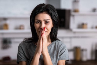 upset woman with bruise on face and praying hands crying at home, domestic violence concept  clipart
