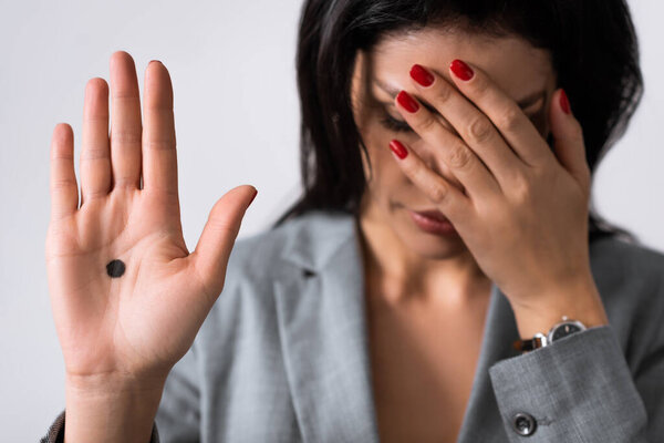 selective focus of sad businesswoman showing hand with black dot on palm and covering eyes isolated on white, domestic violence concept 