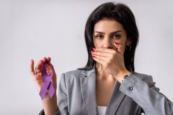 businesswoman covering mouth and holding purple ribbon isolated on white, domestic violence concept 