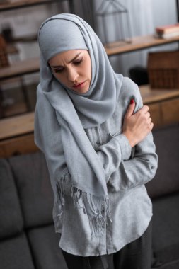 Mutsuz Müslüman kadın oturma odasında koluna dokunuyor, aile içi şiddet kavramı.  