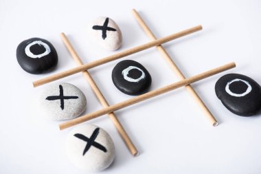 tic tac toe game with grid made of paper tubes, and pebbles marked with naughts and crosses on white surface  clipart