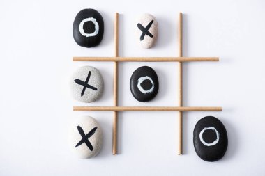 Kağıt tüplerden yapılmış ızgarayla ve beyaz yüzeyde çakıl ve haçlarla işaretlenmiş çakıl taşlarıyla tic tac toe oyununun üst görünümü 