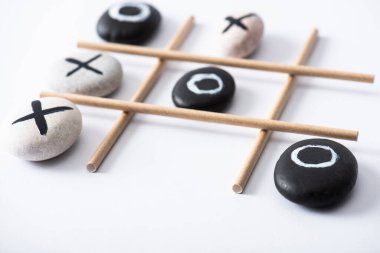 selective focus of tic tac toe game with grid made of paper tubes, and pebbles marked with naughts and crosses on white surface clipart