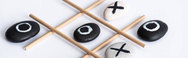 Kağıt tüplerden yapılmış ızgara ve beyaz yüzey üzerinde haç ve çakıl taşları ile panoramik Tic tac toe oyunu