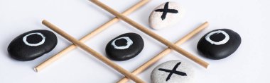 panoramic shot of tic tac toe game with grid made of paper tubes, and pebbles marked with naughts and crosses on white surface clipart