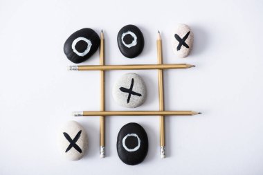 Tic tac toe oyununun üst görünümü kalemlerden yapılmış ızgaralar, ve beyaz yüzeyde haç ve naughts ile işaretlenmiş çakıl taşları