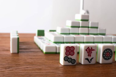 KYIV, UKRAINE - 30 HAZİRAN 2019: Tahta masa üzerindeki mahjong oyun fayanslarından yapılmış sıraların ve piramidin seçici odağı