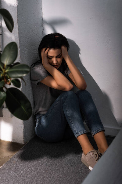 selective focus of scared woman with bruise on face sitting on floor at home, domestic violence concept 