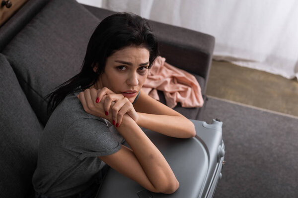 overhead view of sad woman with bruise on face sitting on sofa with suitcase, domestic violence concept 