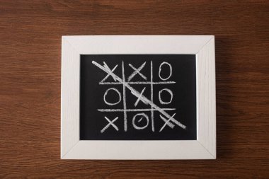 top view of tic tac toe game on blackboard with crossed out row of crosses on wooden surface clipart