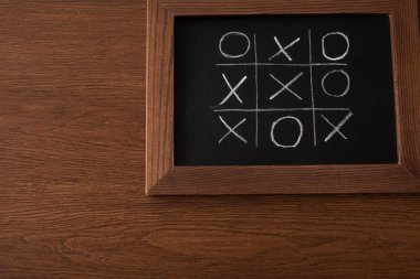 top view of tic tac toe game on blackboard with chalk grid, naughts and crosses on wooden surface clipart