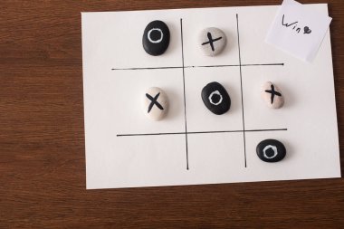 Tic tac toe oyununun üst görünümü. Üzerinde haç ve haç olan taşlar ve tahta yüzey üzerinde galibiyet yazısı olan kart.