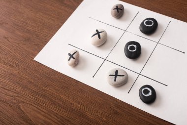 Tahta yüzeyde çakıl taşları ve haçlarla işaretlenmiş beyaz kağıt üzerinde tic tac toe oyunu