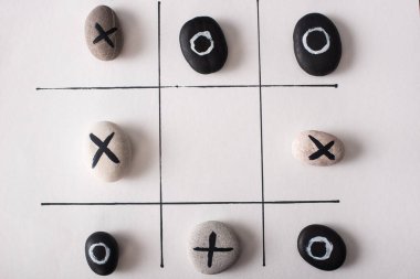 Beyaz kağıt üzerinde haç ve haçlarla işaretlenmiş taşlar ile tic tac toe oyununun üst görünümü
