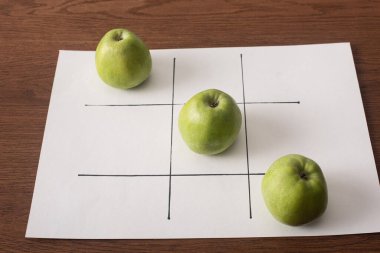 Tahta yüzey üzerinde üç yeşil elma sırasıyla beyaz kağıt üzerinde tic tac toe oyunu