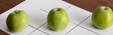 panoramik shote of tic tac toe game on white paper and row of three green apple on wood face