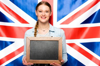 smiling pretty girl with braid holding empty chalkboard on uk flag background