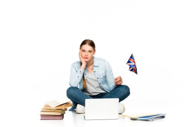 Üzgün kız dizüstü bilgisayarı, kitapları ve kitaplarıyla yerde oturuyor ve beyaz üzerinde Birleşik Krallık bayrağı taşıyor.