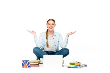 happy girl sitting on floor with laptop, books and copybooks, uk flag and gesturing isolated on white clipart