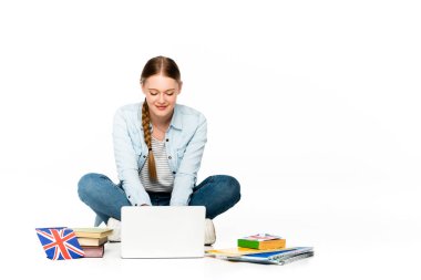 gülümseyen kız dizüstü bilgisayarla kitapların ve kitapların yanında oturuyor, Birleşik Krallık bayrağı beyaz üzerine izole edilmiş.