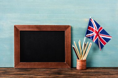Kalemlerin yanındaki boş karatahta ve mavi duvarın yanındaki ahşap masada İngiliz bayrağı