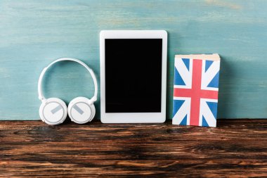 Kulaklıklar, boş ekranlı dijital tablet ve mavi duvarın yanındaki tahta masada İngiliz bayrağı.