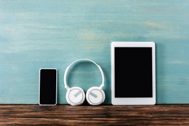 Kulaklıklar, dijital tablet ve akıllı telefon mavi duvarın yanındaki ahşap masada.