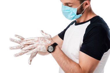 Tıbbi maskeli bir adam beyaz sabunlu ellere bakıyor. 