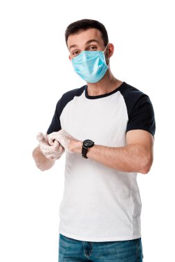 Tıbbi maskeli bir adam ellerini yıkıyor ve beyaz kameraya bakıyor. 