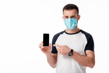 Tıbbi maskeli adam beyaz ekranlı akıllı telefonu işaret ediyor. 