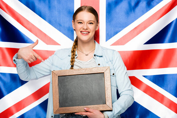 smiling pretty girl with braid pointing at empty chalkboard on uk flag background