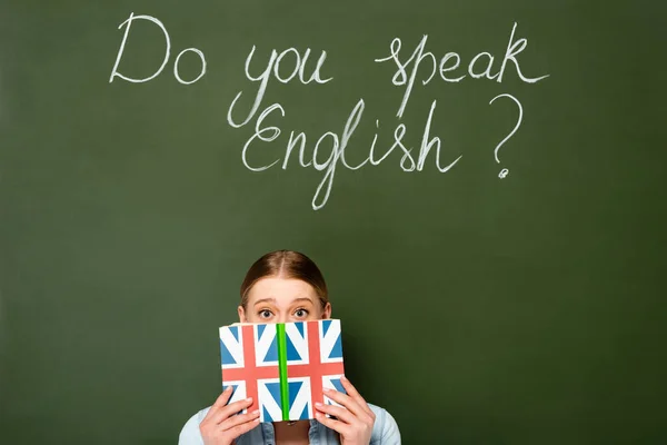 漂亮的女孩 脸色苍白 拿着写有英国国旗的书靠近黑板你会说英语吗 — 图库照片