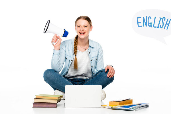 smiling girl sitting on floor with loudspeaker near laptop, books and copybooks, English lettering in speech bubble isolated on white