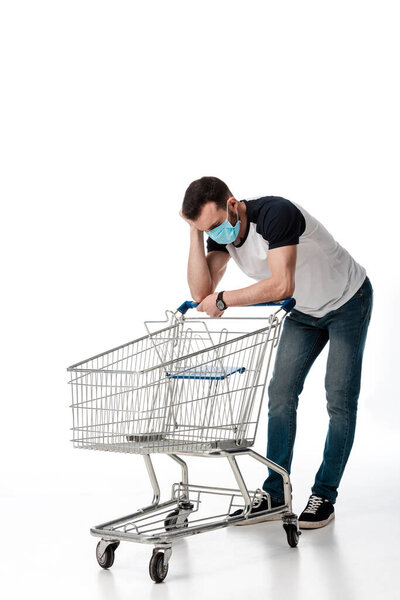 man in medical mask looking at empty shopping cart on white