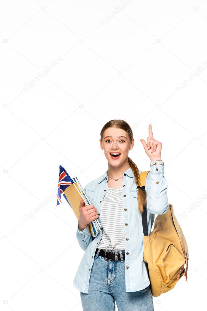 excited girl with backpack pointing up and holding copybooks and uk flag isolated on white