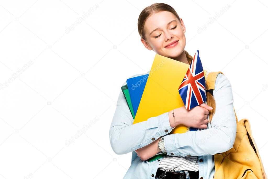 smiling girl with backpack and closed eyes holding copybooks and uk flag isolated on white