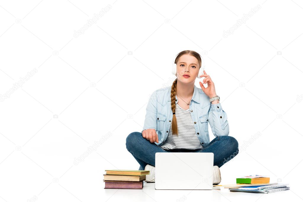 girl sitting on floor in headphones near laptop, books and copybooks isolated on white