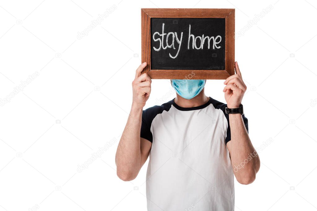 man in medical mask covering face while holding chalk board with stay home lettering isolated on white 