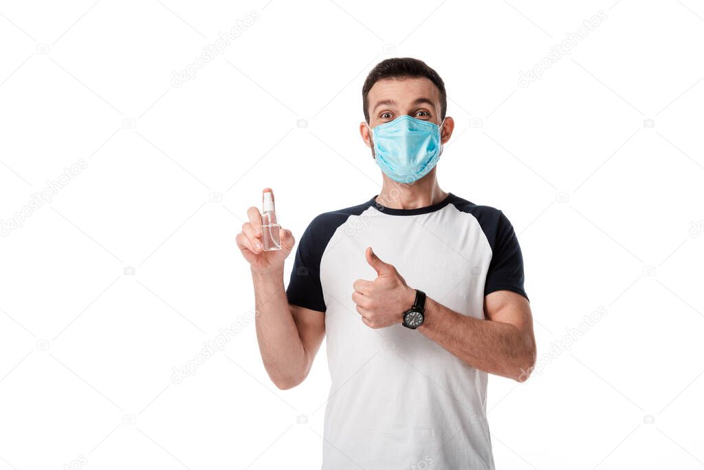 man in medical mask holding spray bottle with hand sanitizer and showing thumb up isolated on white 