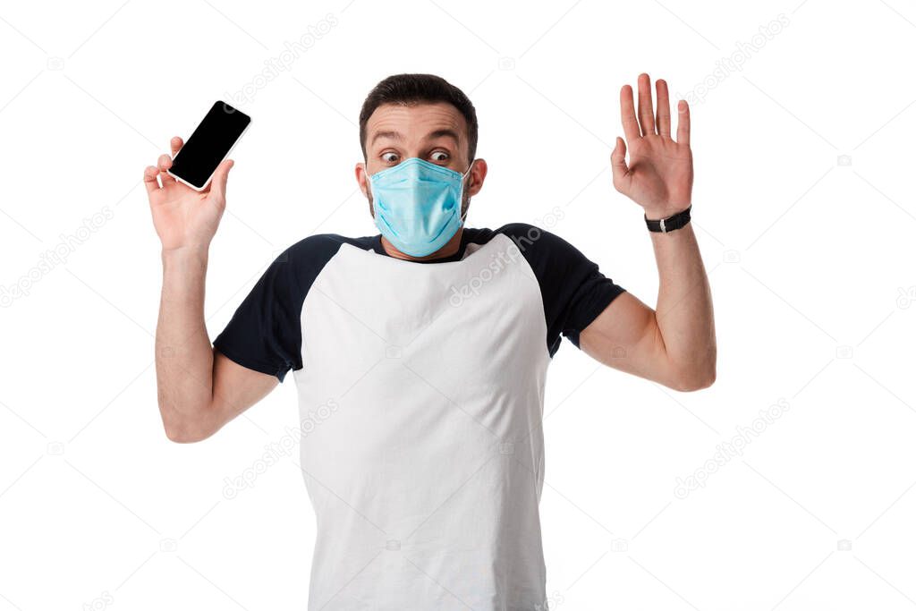 shocked man in medical mask holding smartphone with blank screen and putting hands up isolated on white 