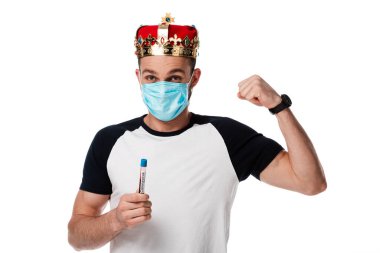 Tıbbi maskeli ve taç takmış bir adam elinde Coronavirus kan örneğiyle test tüpü tutuyor ve yumruğunu beyazın üzerinde gösteriyor. 